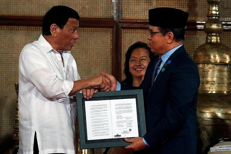 President Rodrigo Duterte presenting a document containing a signed autonomy law to Moro Islamic Liberation Front chairman Murad Ebrahim during a ceremony in Manila yesterday.