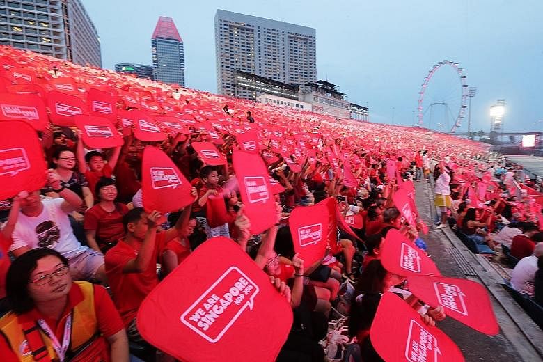 The audience (right) taking part in the Placard Challenge, where they used the red and white placards in their funpacks to form the words "We Are Singapore" across the floating platform. Performers from the People's Association (far right) raising ex