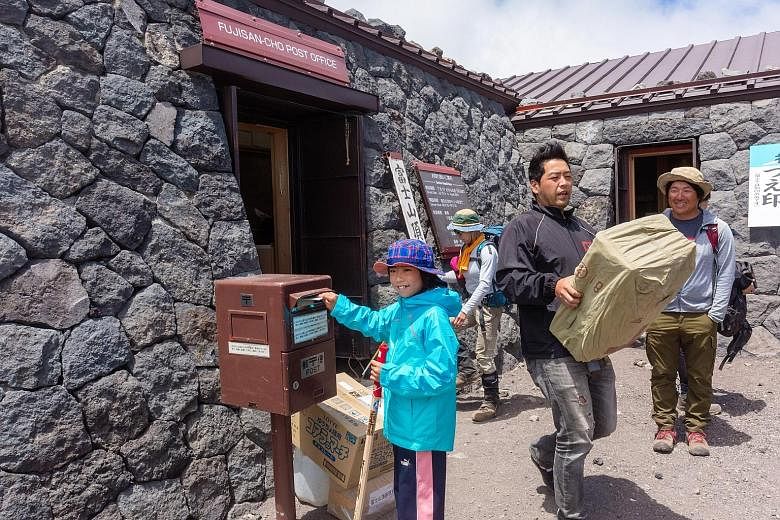 A young hiker uses a mailbox outside the post office on the summit of Mount Fuji in Fujinomiya, Japan.