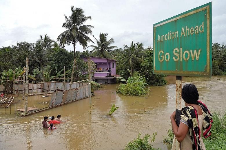 Residents wading through a flooded street next to marooned houses on the outskirts of Kerala's northern Kozhikode district. With thousands still trapped in flooded areas, power and communication lines down and fresh alerts of further torrential rain,