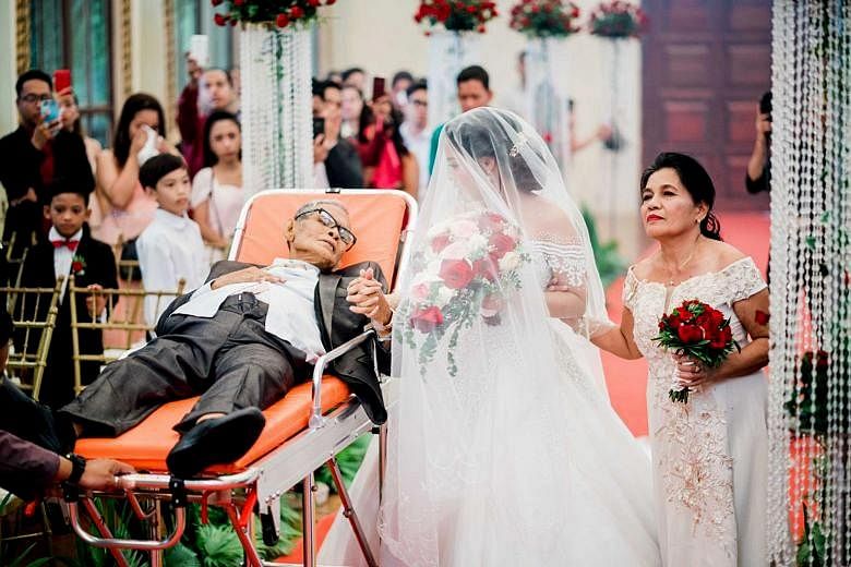 Ms Charlotte Gay Villarin has her fingers laced around those of her father - Mr Pedro Villarin - who, despite being weak, looks lovingly at his daughter from a stretcher, which is being pulled down the aisle. On the right is the bride's mother.