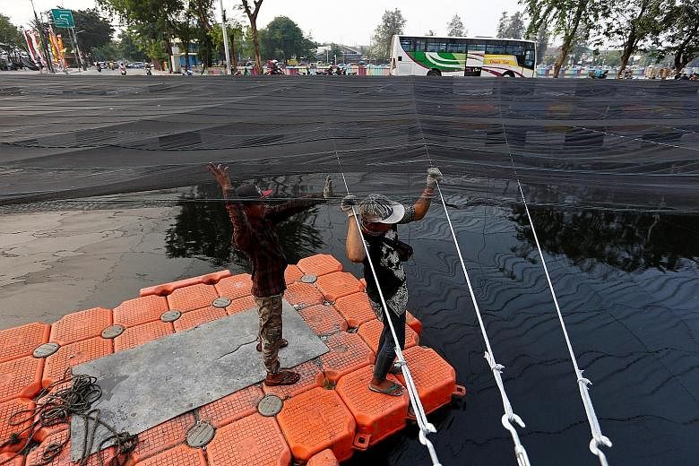 Workers on a makeshift raft installing nets last month to cover a polluted river beside the Athletes' Village at Kemayoran district in Jakarta. The country has spared no effort to ensure a successful Games.