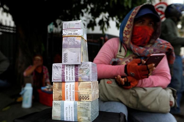 A woman who provides change for large banknotes with stacks of Indonesian rupiah on a street in Jakarta. The currency has lost nearly 8 per cent of its value against the US dollar since the beginning of the year. And this month, the Bank of Indonesia
