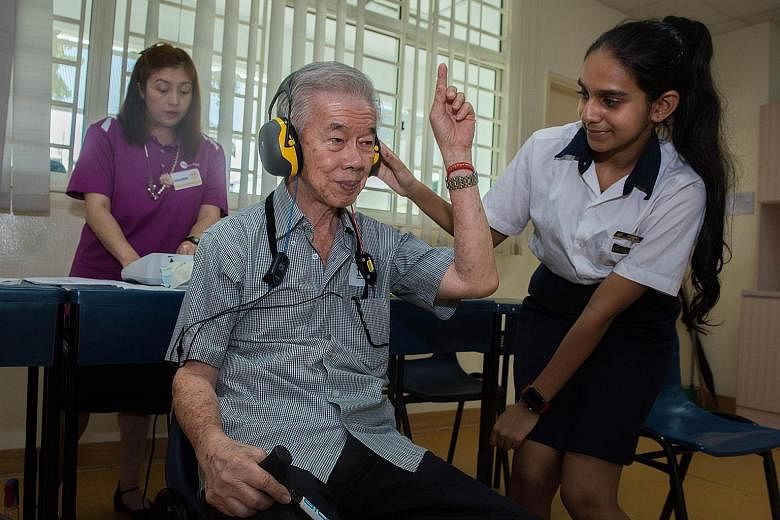 Secondary 2 student Raksha Narayan Rao helping Mr Koh Tiong San, 74, during his hearing check, which was conducted by Ms Mildred Tan (in purple) from a healthcare provider.
