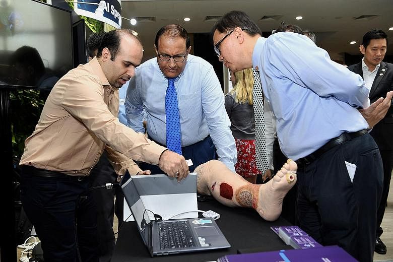 Minister for Communications and Information S. Iswaran (centre) and AI Singapore executive chairman Ho Teck Hua observing a demonstration of artificial intelligence by Dr Hossein Nejati, chief technology officer of health tech start-up KroniKare, whi