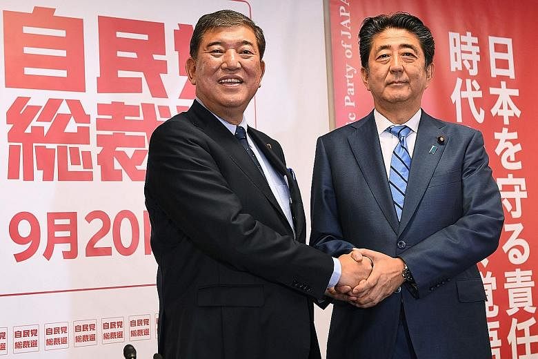 Mr Shinzo Abe (near left) and former defence minister Shigeru Ishiba shaking hands before their joint press conference yesterday. Both are running for Liberal Democratic Party president. As the LDP is the ruling party, its president is the de facto J
