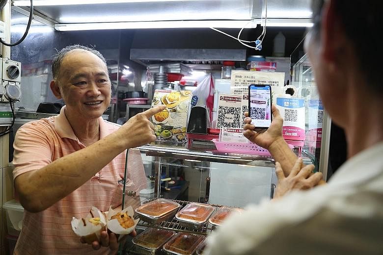 Hawker Christopher Lau with a customer making payment using the Nets QR code at his bakery stall at Old Airport Road Food Centre. Mr Lau's stall has three QR codes to accept payments from three different e-wallets. He says he is looking forward to Ne