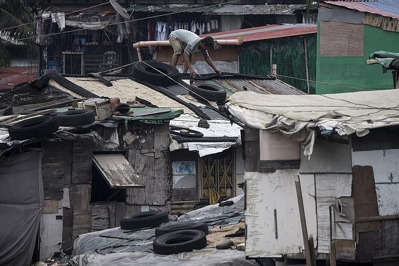A resident reinforcing the roof of his house with heavy tyres in a Manila slum area yesterday, with Super Typhoon Mangkhut expected to make landfall on northern Luzon early today (Singapore time). Thousands of Filipinos fled their homes and stockpile