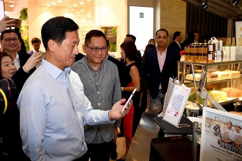 Mr Ong Ye Kung, Education Minister and MAS board member, making payment via the SGQR code at a Toast Box outlet yesterday. With him is Mr Vincent Lim, regional general manager for Toast Box. For consumers, SGQR means more chances that the cashless sc