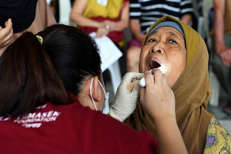 Madam Sudiah Sapii, 76, getting her teeth checked by a volunteer at a health screening yesterday at Kampung Admiralty, where Project Silver Screen was launched. Around 200 people from the neighbourhood took the chance to have their vision, hearing an