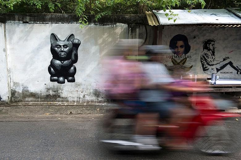 A caricature by street artist Headache Stencil of Thailand's junta chief - depicted as "a lucky cat" with a paw raised to rake in money - is spotted on a wall on Sept 4. Headache's work has caught the imagination of a country where an increasing numb