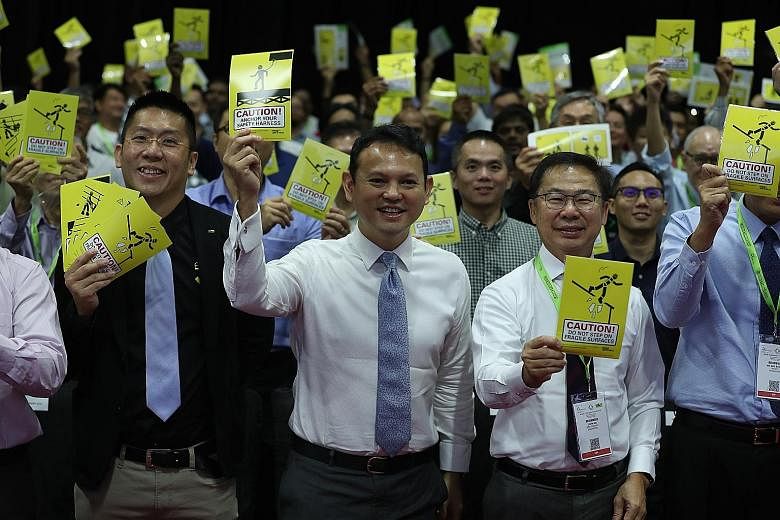 Minister of State for Manpower Zaqy Mohamad, flanked by the International Powered Access Federation's South-east Asia regional general manager Raymond Wat (left) and Workplace Safety and Health Council chairman John Ng, holding up stickers containing