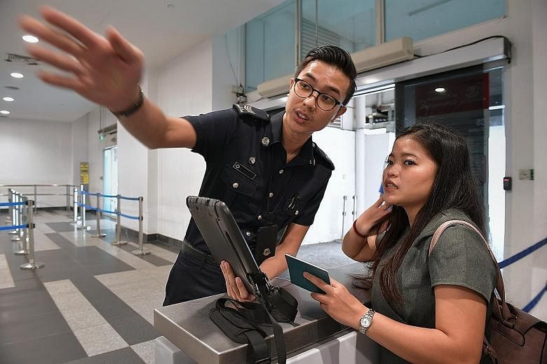Indonesian tourist Indah, 21, receives help from an officer of the Immigration and Checkpoints Authority (ICA), Sergeant Muhammad Fazril, on using an electronic arrival card instead of the paper disembarkation/embarkation card to provide her personal