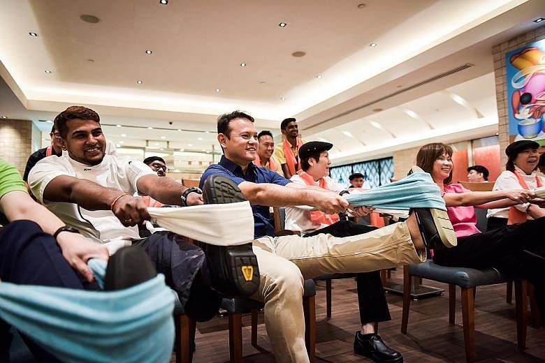 Minister of State for Manpower and National Development Zaqy Mohamad (in blue) and Senior Minister of State for Health Amy Khor (in pink), who co-chair a committee on workplace safety and health, participating in a stretching exercise with workers fr