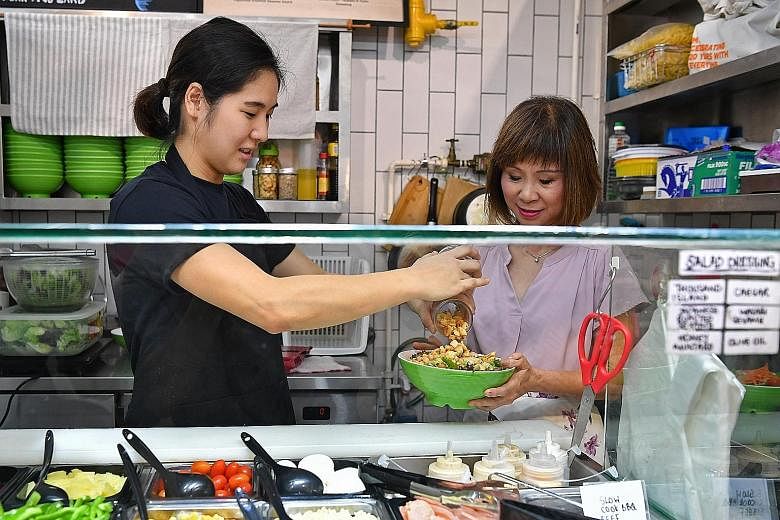 Ms Poh Ying Min (left), who runs a customised salad bowl stall at Block 163 Bukit Merah Central Food Centre under the Incubation Stall Programme, making a bowl of salad for Senior Minister of State for the Environment and Water Resources Amy Khor yes