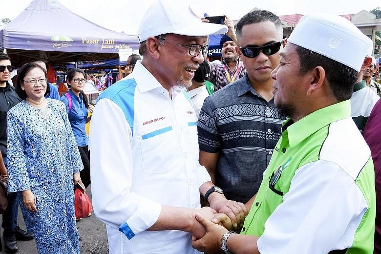 Datuk Seri Anwar Ibrahim (left) greeting Parti Islam SeMalaysia candidate Mohd Nazari Mokhtar while campaigning at the Bagan Pinang Farmers' Market in Port Dickson.