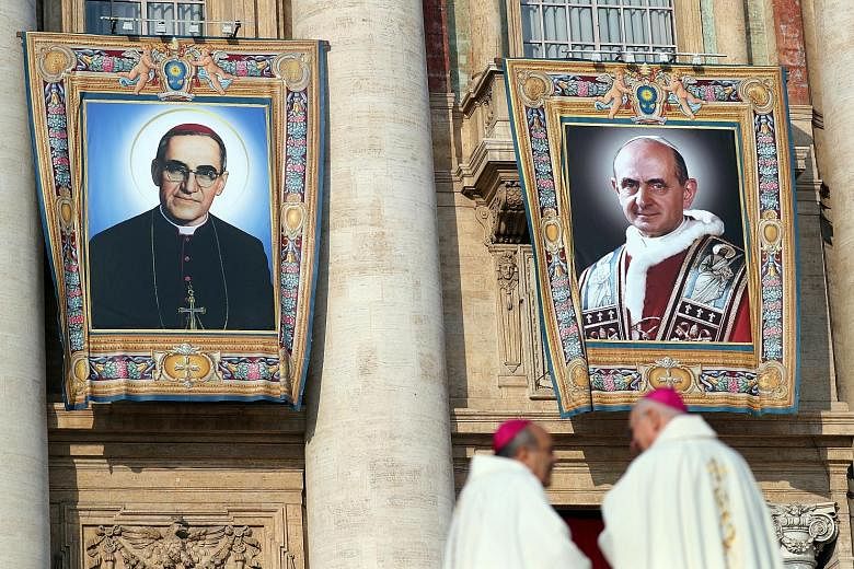 Images of Pope Paul VI (left) and El Salvador's Archbishop Oscar Romero put up ahead of a ceremony before tens of thousands of people in St Peter's Square in Vatican City yesterday, in which Pope Francis declared the two men saints, along with five o