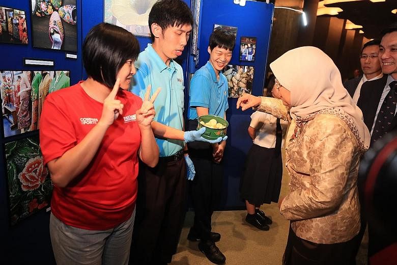 Mr John Ngu Dao Xin offering President Halimah Yacob cookies made by trainees from APSN Centre for Adults and YMCA volunteers. With him are Ms Lun Ting Yuan and Mr Ling Lee Min. Nineteen special needs staff and beneficiaries from YMCA helped to host 
