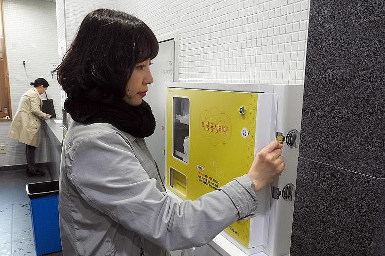 A Seoul government official inserts a gold coin into a dispenser to get a free sanitary pad inside a toilet at the Seoul Metropolitan Library. Concerns about the public abusing the free service were unfounded, judging from the number of pads taken.