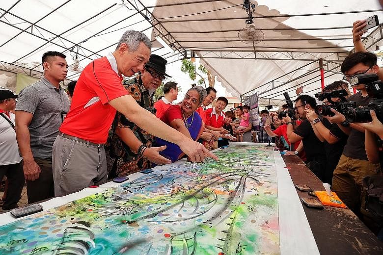 Prime Minister Lee Hsien Loong discussing the details of an artwork at a family carnival during yesterday's tree-planting event. He also opened a new sheltered linkway for residents of Fern Spring and Fern View estates.
