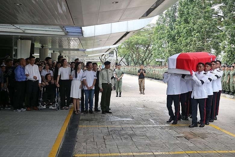 Corporal First Class (CFC) Liu Kai's father (front row, second from left), mother, and two sisters hold hands as they watch pallbearers carry his casket into the service hall at Mandai Crematorium. Hundreds of servicemen lined the driveway for the mi