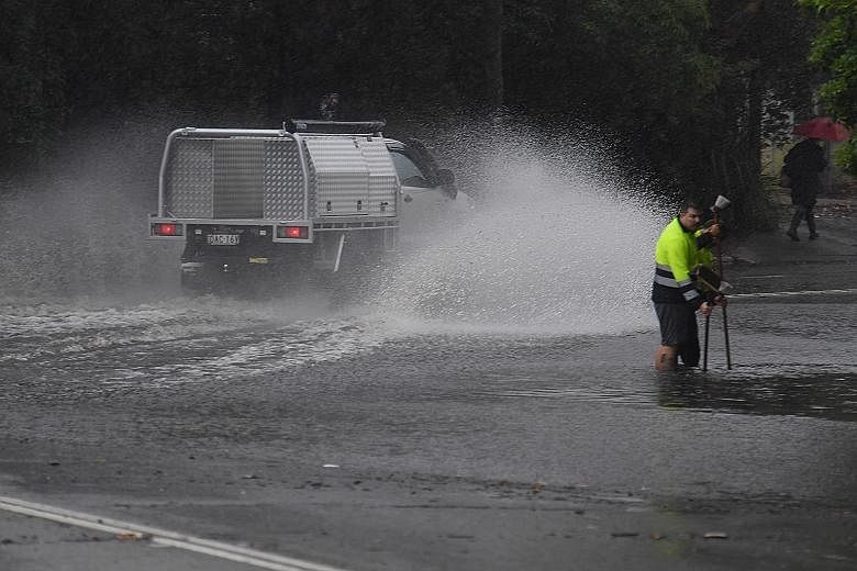 Workers trying to clear a drain, as a vehicle splashes through floodwaters on Railway Terrace during rainy weather in Sydney yesterday, when the city received more than a month's worth of rain in just two hours.