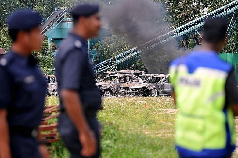 Policemen at the site of the Maha Mariamman Temple, where a riot broke out on Monday. In the background are some cars that were badly burnt in the incident. Prime Minister Mahathir Mohamad warns that those responsible will face stern action.