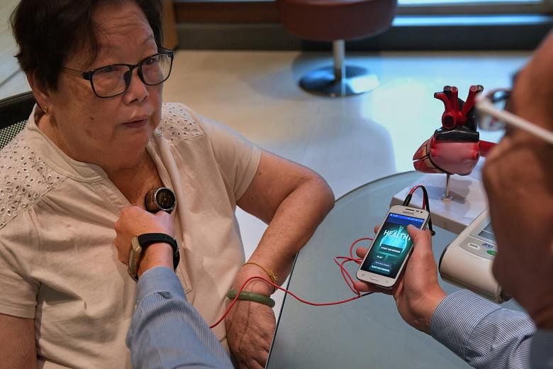 Tan Tock Seng Hospital's head of cardiology David Foo demonstrating the use of the device - which checks for fluid accumulation in the lungs, an early symptom of heart failure - to heart patient Tan Hui Keng at the hospital yesterday. The device was 
