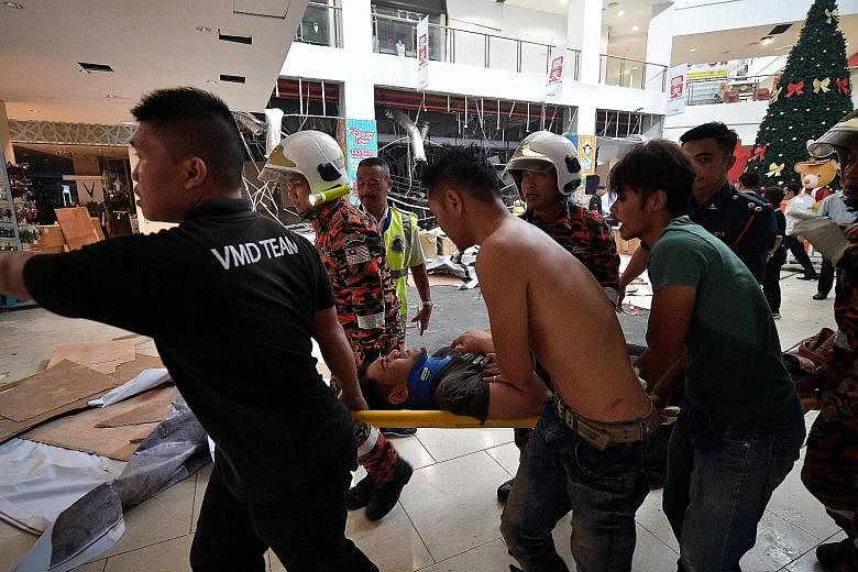 (Above) Investigators and firefighters at the scene after an explosion at the CityOne Megamall in Kuching, Sarawak, yesterday which killed three men. (Below) One of the injured being rushed to hospital. Of the 26 injured, four are in critical conditi