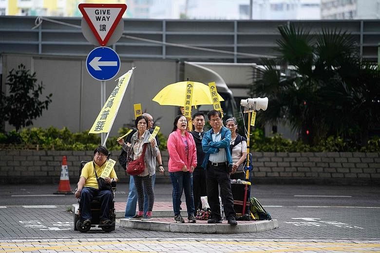 Cardinal Joseph Zen (above) said he felt "ashamed" that he did not endure the pepper spray and tear gas that many demonstrators faced during the 2014 rallies. A small group of pro-democracy activists (below) protesting outside the West Kowloon Magist