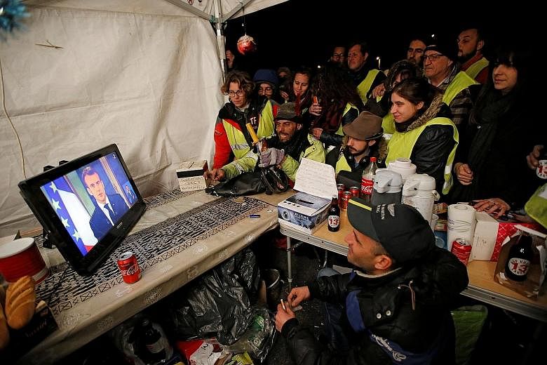 Protesters in yellow vests watching French President Emmanuel Macron on a TV screen at the motorway toll booth in La Ciotat, near Marseille, on Monday. The President's popularity has fallen since he came to power in May last year, with critics saying