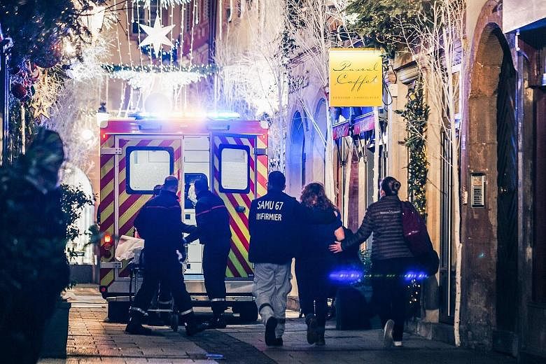 (Top) Paramedics treating an injured person on a street in Strasbourg after the shooting on Tuesday. (Above) French special police force members patrolling the French-German border yesterday. Emergency workers escort a woman after the shooting near t