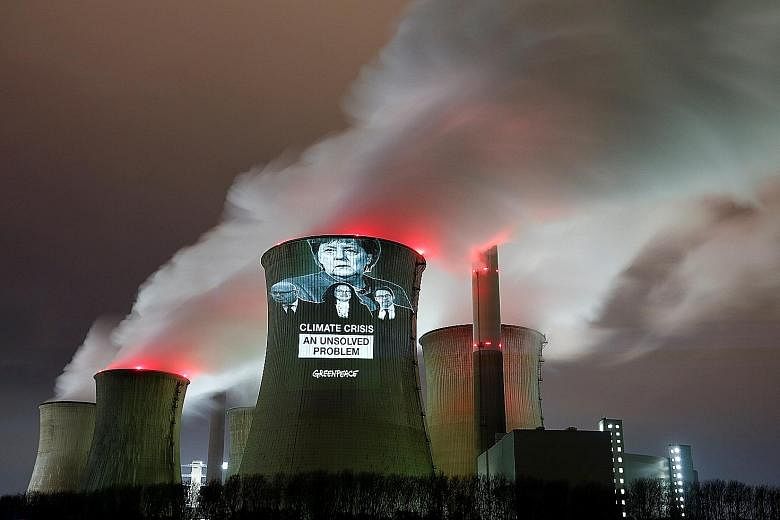 Images of German Chancellor Angela Merkel (top), and (from left) German Economy Minister Peter Altmaier, Social Democratic Party chairman Andrea Nahles and German Transport Minister Andreas Scheuer projected by Greenpeace activists on a cooling tower