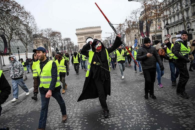 People in yellow vests marching yesterday near the Arc de Triomphe in Paris, to protest against President Emmanuel Macron's economic policies. Tear gas was fired at small groups of protesters in brief clashes with riot police near the Champs-Elysees,