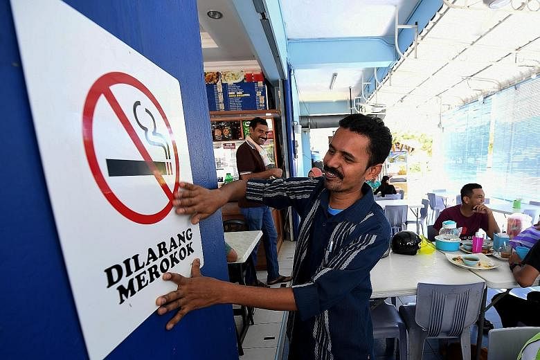 An employee of an eatery in Sandakan, Sarawak, putting up a no-smoking sign on Tuesday, the day the ban kicked in.
