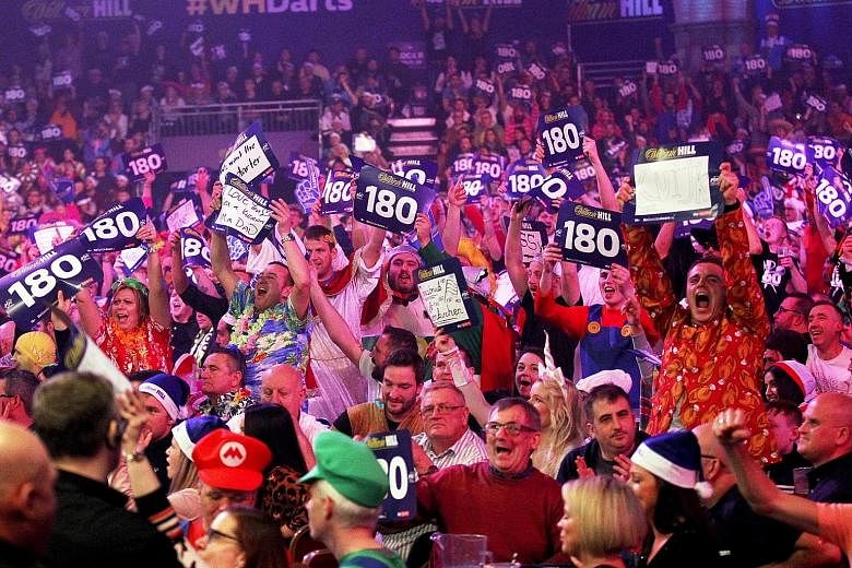 Above: Fans reacting during the PDC World Championship final between Briton Michael Smith and Dutchman Michael van Gerwen at the Alexandra Palace in north London, on Tuesday. Left: Van Gerwen celebrating as pyrotechnics ignite after he beat Smith 7-3