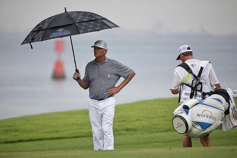 Dru Love approaches his putt on the eighth hole during the first round of the SMBC Singapore Open yesterday. He shot a two-over 73. Davis Love III shielding himself from the rain on the seventh hole yesterday. He was three under through 11 holes for 
