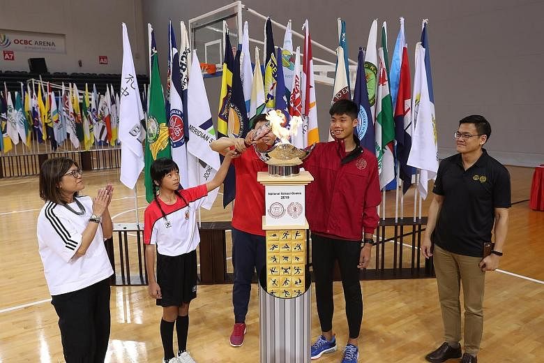 Tia Foong Po Shiun (left) from Haig Girls' School's football team and Victoria Junior College's high jumper Kampton Kam jointly lighting the torch with Senior Minister of State for Education Chee Hong Tat at yesterday's opening of the National School