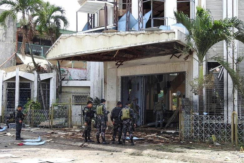 Policemen and soldiers outside the wrecked church in Jolo, Sulu province, which was hit by two bomb attacks on Sunday. Security officials have tagged six "persons of interest" from the Ajang-ajang faction of the Abu Sayyaf as the main suspects.