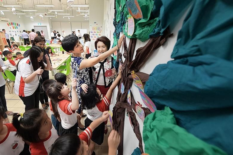 Second Minister for Finance and Education Indranee Rajah and Senior Parliamentary Secretary for Education and Manpower Low Yen Ling helping children from Big Heart Student Care centre in Lianhua Primary School put up notes of appreciation on a "tree"