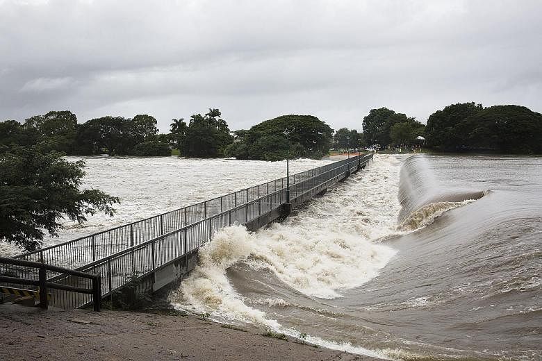 Floodwaters at Aplins Weir in Townsville on Friday. The local authorities issued a number of flood warnings yesterday morning. People wading in floodwaters in Townsville on Friday. Residents were told to leave their homes as Queensland's flood disast