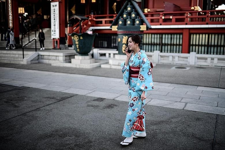 A woman using a mobile phone in Tokyo's Asakusa district. Japan's three telcos are conducting 5G mobile communications trials. A 5G service robot serving bottles of water to travellers at a Hangzhou railway station during the Spring Festival travel r