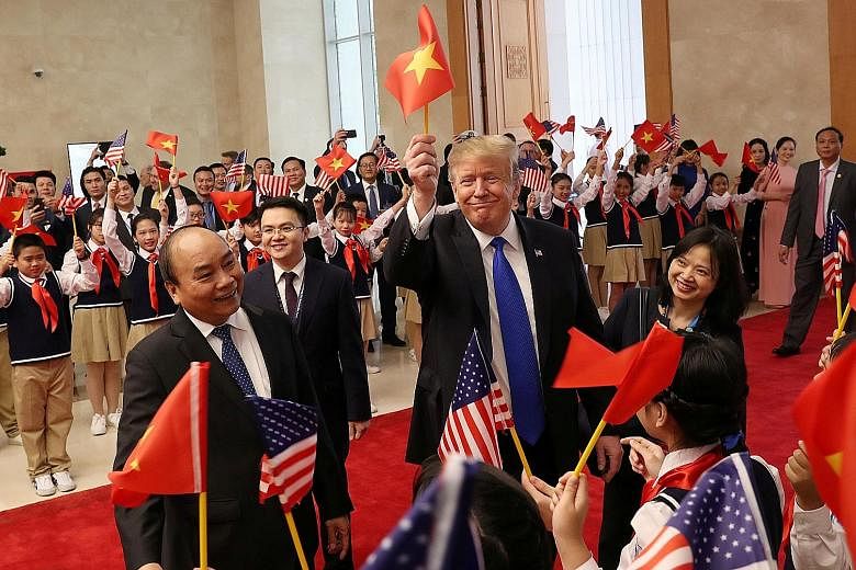 US President Donald Trump waving a Vietnamese flag as he is greeted by students during a meeting with Vietnamese Prime Minister Nguyen Xuan Phuc (left, foreground) in Hanoi yesterday.