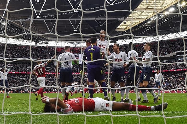 Tottenham Hotspur goalkeeper Hugo Lloris celebrating with teammates after saving a penalty from Arsenal's Pierre-Emerick Aubameyang (front) during their EPL match at Wembley Stadium yesterday which ended 1-1.
