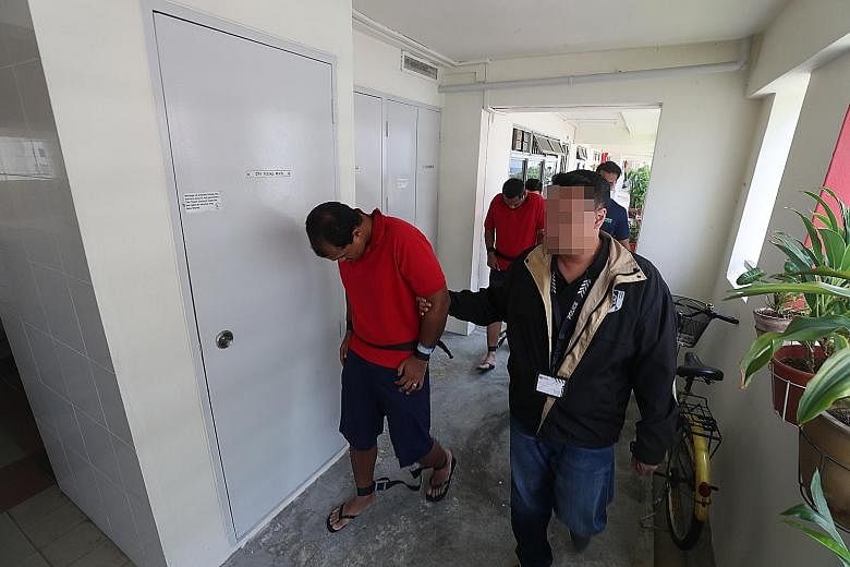 Mohamed Fauzi Abdul Rahman (front) and Mohammad Zahan Saad being taken by police officers on Friday to a Woodlands flat, where they allegedly burned the front door and a pair of slippers outside the apartment.