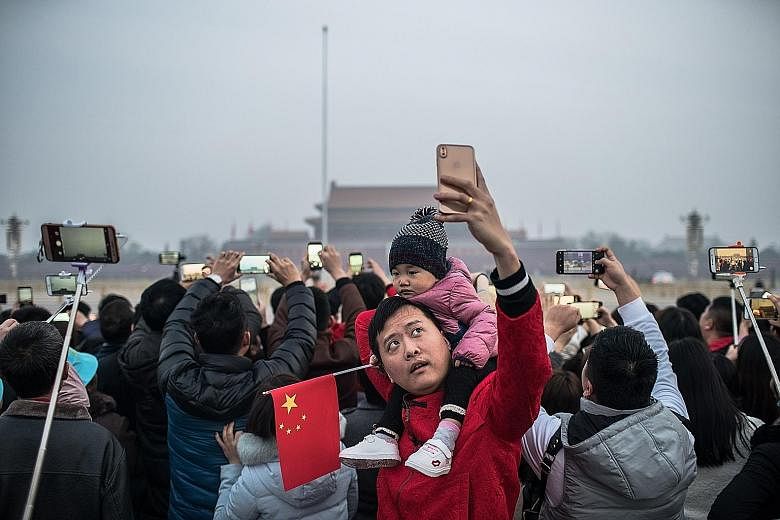 Delegates and journalists attending the National People's Congress held at the Great Hall of the People in Beijing yesterday. People taking photos while waiting for the flag-raising ceremony at Tiananmen Square before the NPC's opening yesterday.