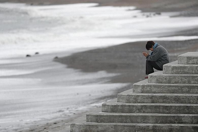 A woman facing the sea to pray while mourning the victims of the 2011 earthquake, tsunami and nuclear disaster in Japan that left about 18,500 people dead or missing.