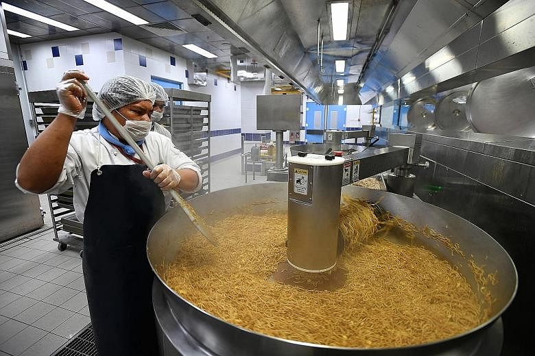 Members of Sats' kitchen crew dishing nasi goreng (above) into the thermoforming line to extend the shelf life of the food, and using an auto-fryer to cook a large batch of noodles (left) in the extended kitchen facility at Changi North.