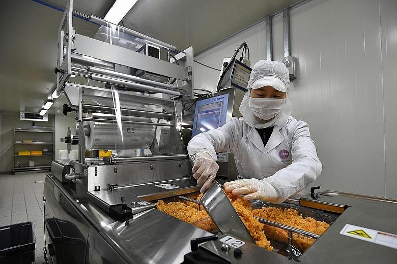Members of Sats' kitchen crew dishing nasi goreng (above) into the thermoforming line to extend the shelf life of the food, and using an auto-fryer to cook a large batch of noodles (left) in the extended kitchen facility at Changi North.