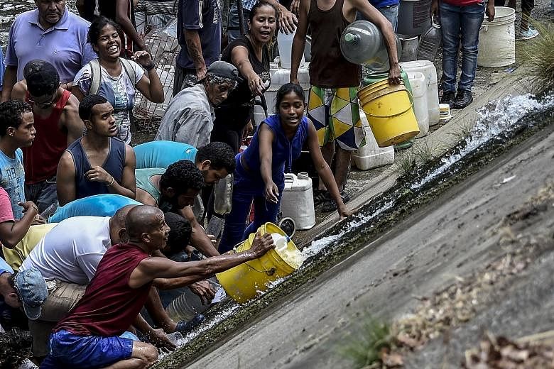 Caracas residents scrambling to collect water from a burst water pipe that is flowing into a sewage canal at the Guaire River.